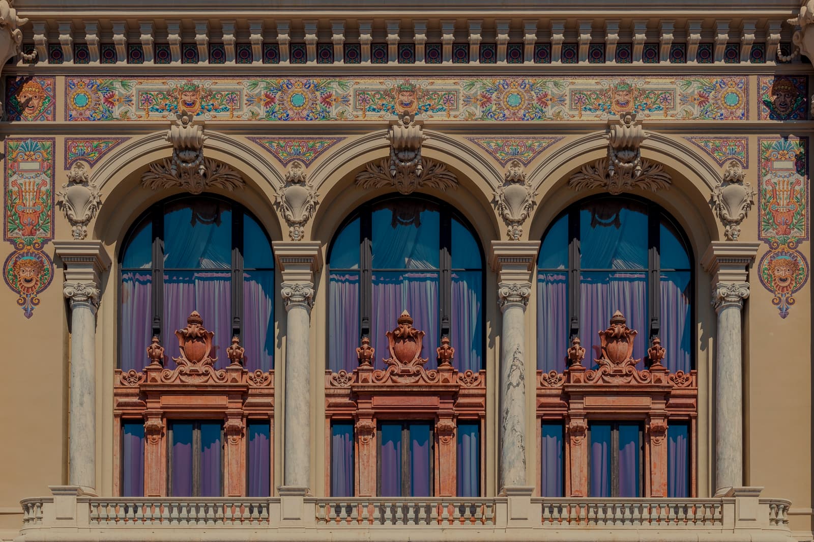 Three tall arched windows on a Belle Epoque façade in Monte-Carlo, set between marble columns under bands of painted ceramic ornament.