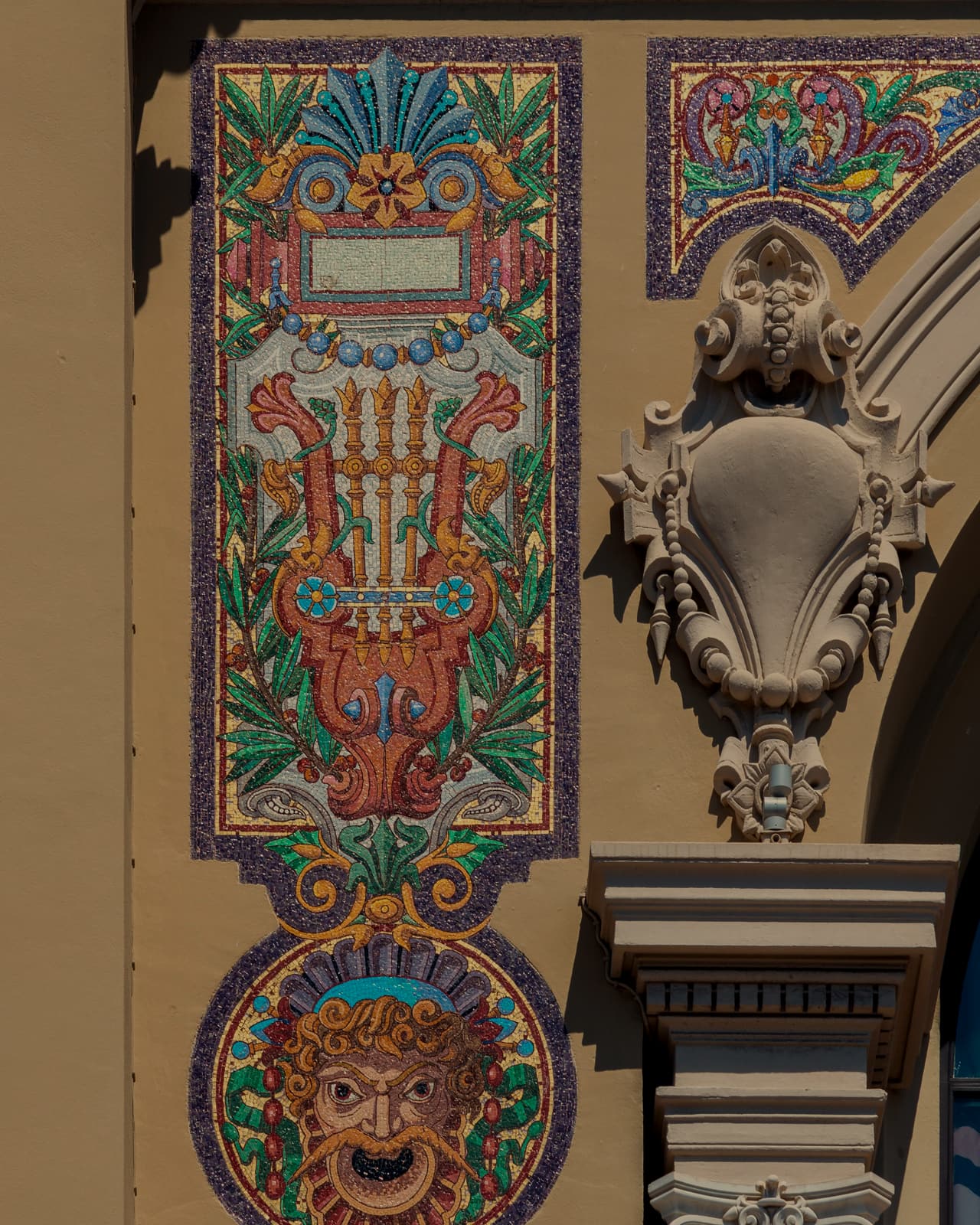 A Belle Epoque mosaic panel of a lyre and a theatrical mask beside a carved stucco cartouche and a column capital.
