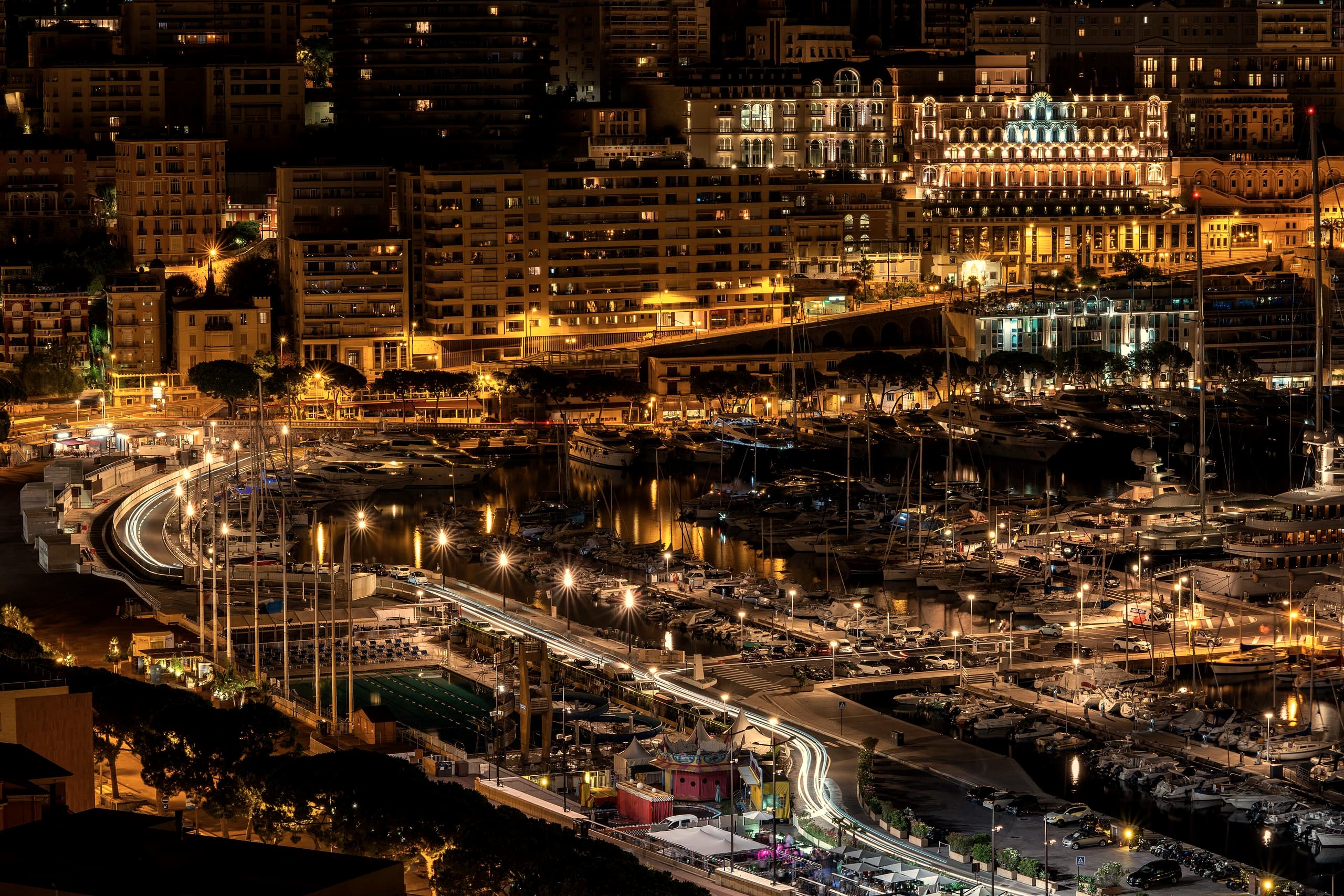 Port Hercule at night seen from above, lit quays and moored yachts beneath the warm windows of Monte-Carlo and its Belle Epoque hotels.