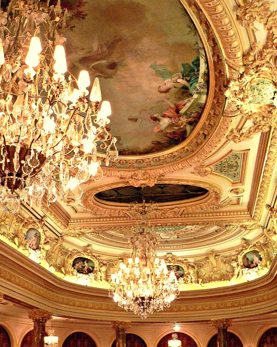 A painted and gilded ceiling hung with crystal chandeliers, glowing above a row of red arches.