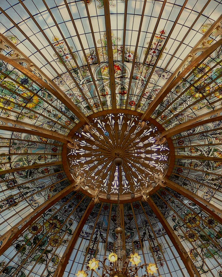 Looking straight up into a stained glass dome, its iron ribs radiating from a gilded centre.