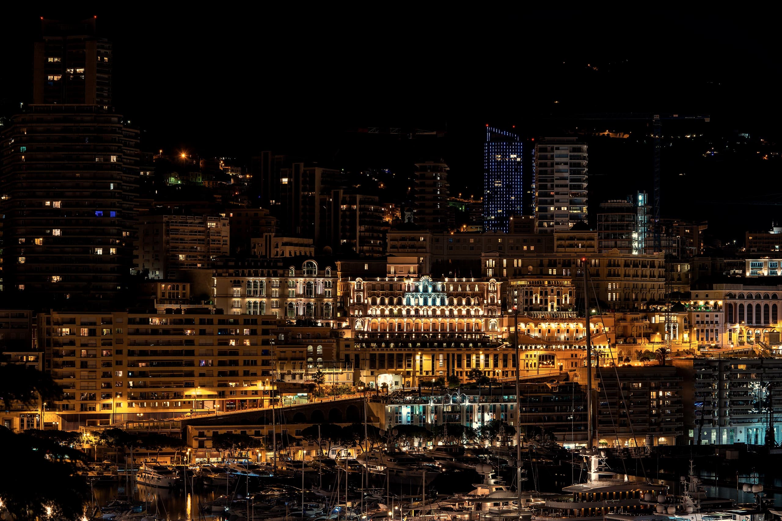 Monte-Carlo at night, apartment buildings and Belle Epoque façades lit gold above the harbour.